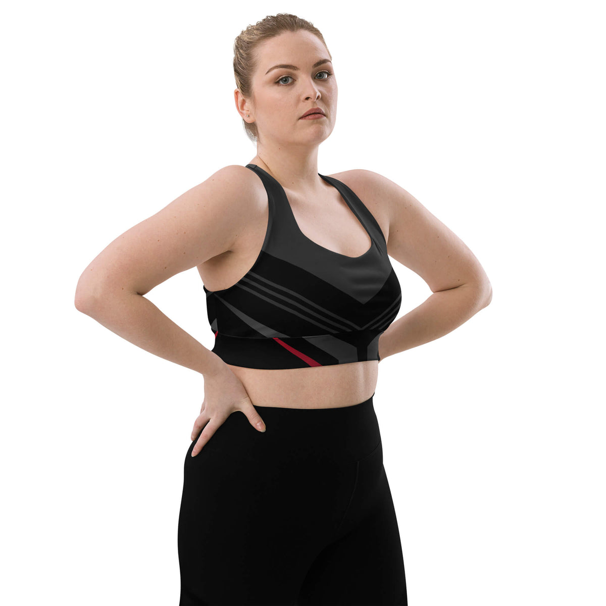 Schräge Vorderansicht des schwarz-anthrazitfarbenen Longline-Sport-BHs am Model mit Händen an der Hüfte